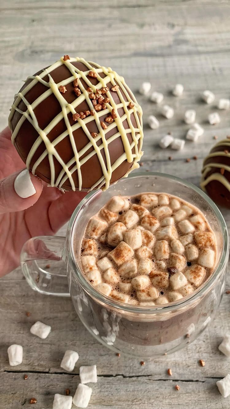 Chocolate hot cocoa bomb held over a mug of hot chocolate with marshmallows