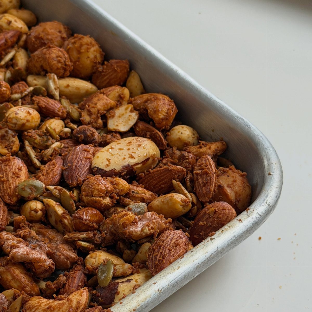 Roasted spiced nuts with almonds and cashews in a silver baking tray.