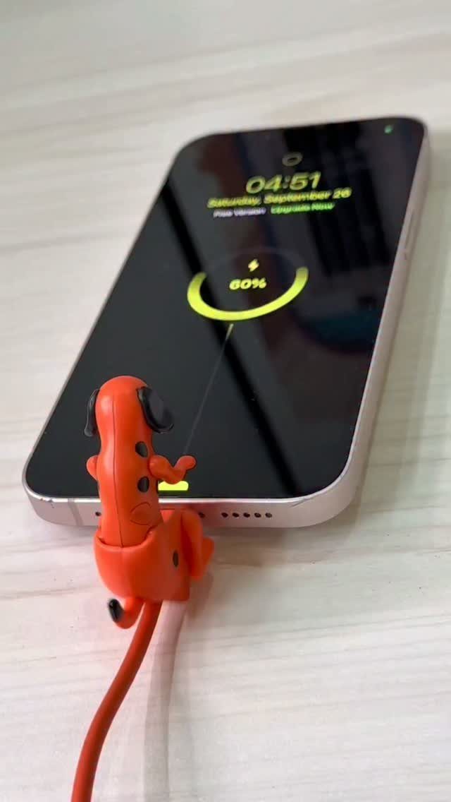 Orange silicone dog cable protector biting a gold smartphone during charging.