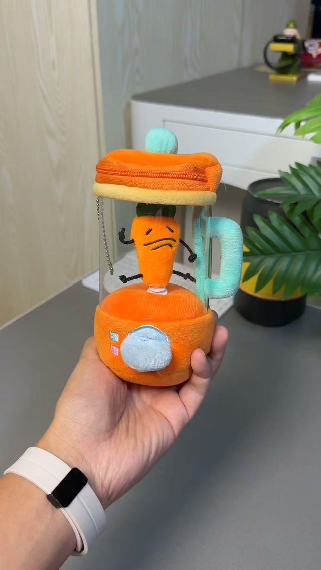 Plush blender toy with a cartoon carrot character inside held by a hand.