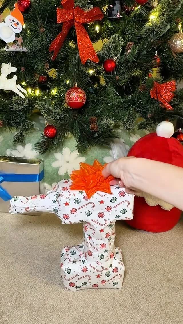 Toilet-shaped gift wrapped in festive paper with an orange bow before a Christmas tree