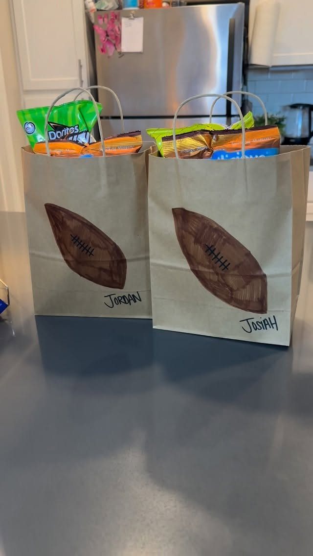 Two brown paper gift bags filled with snacks, decorated with football drawings and names.
