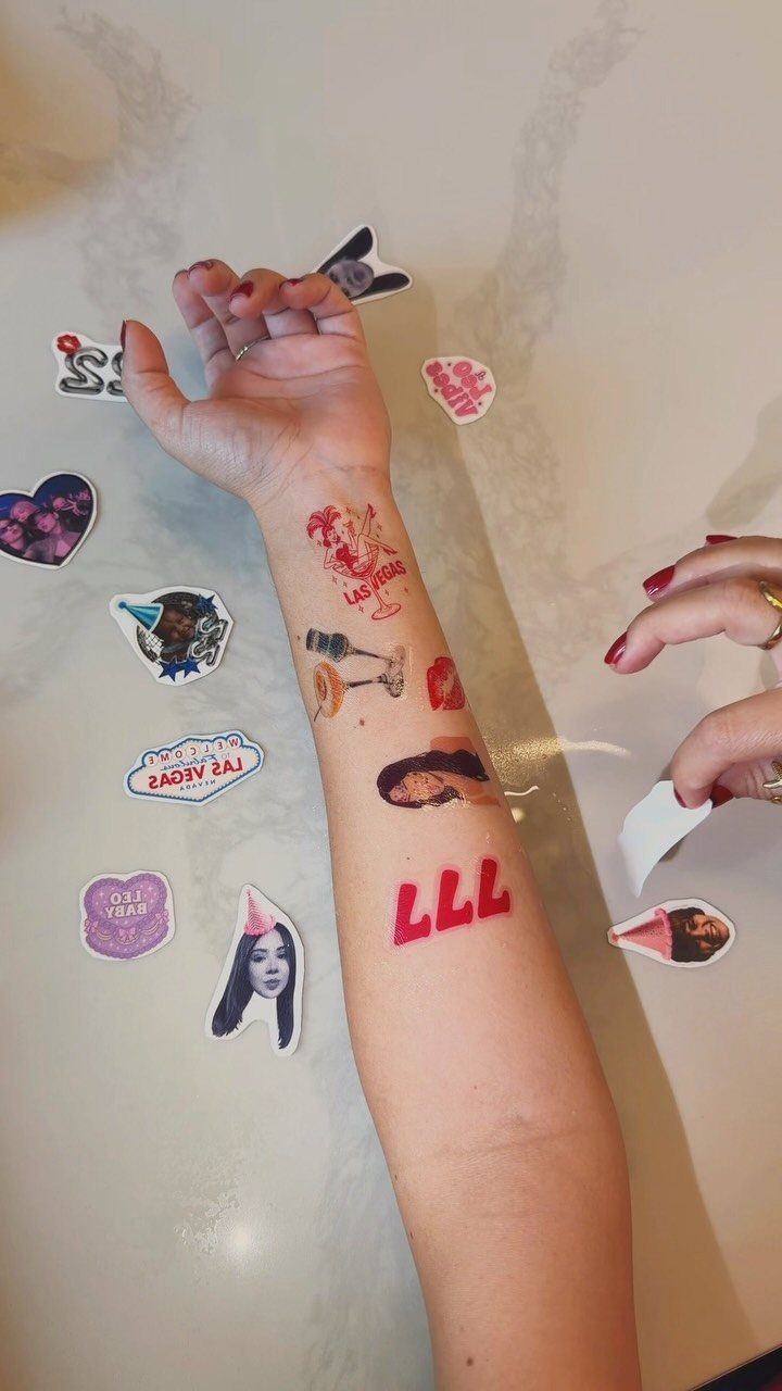 Forearm with colorful temporary tattoos and unapplied stickers on a white marble surface.