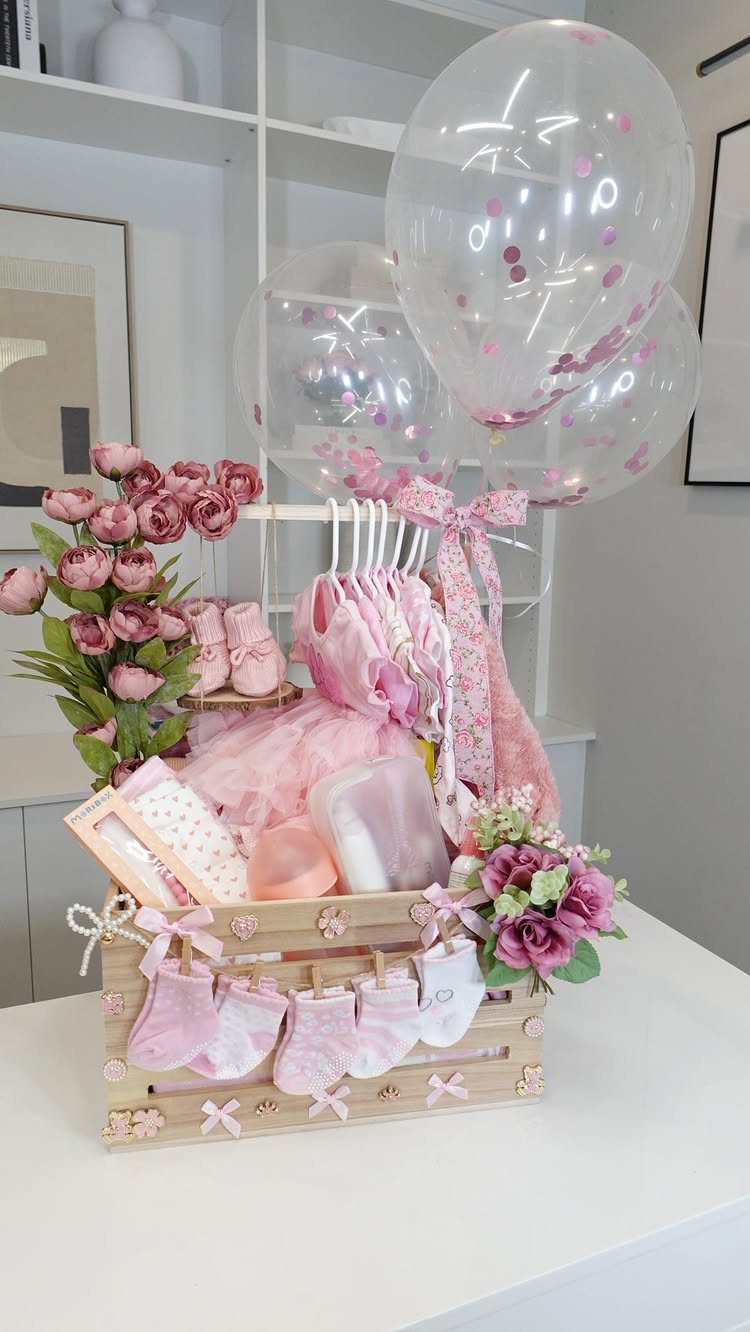 Wooden baby gift crate with pink clothes, socks, roses, and confetti balloons.