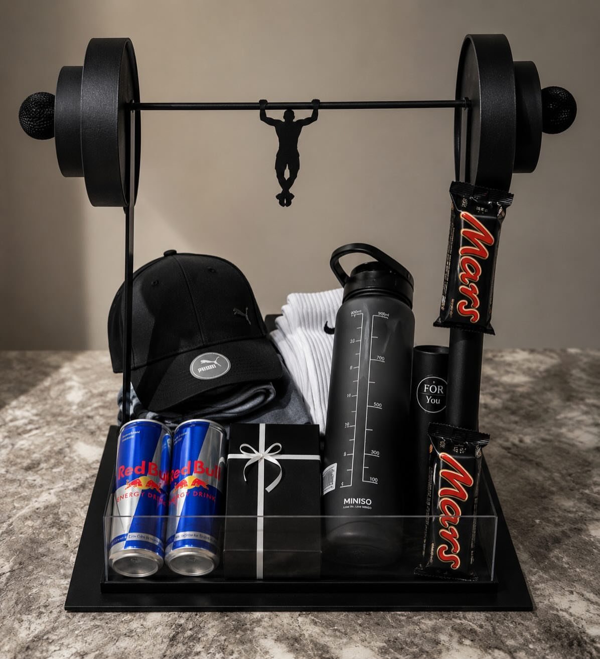 Fitness gift set with barbell frame, water bottle, energy drinks, and gym accessories.