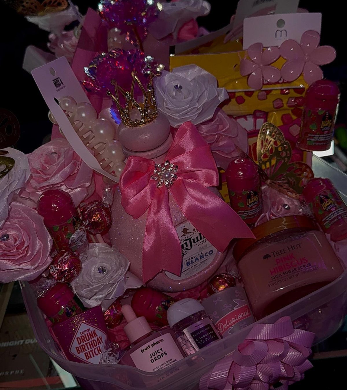 Pink themed gift basket with beauty products, roses, and a crowned bottle.