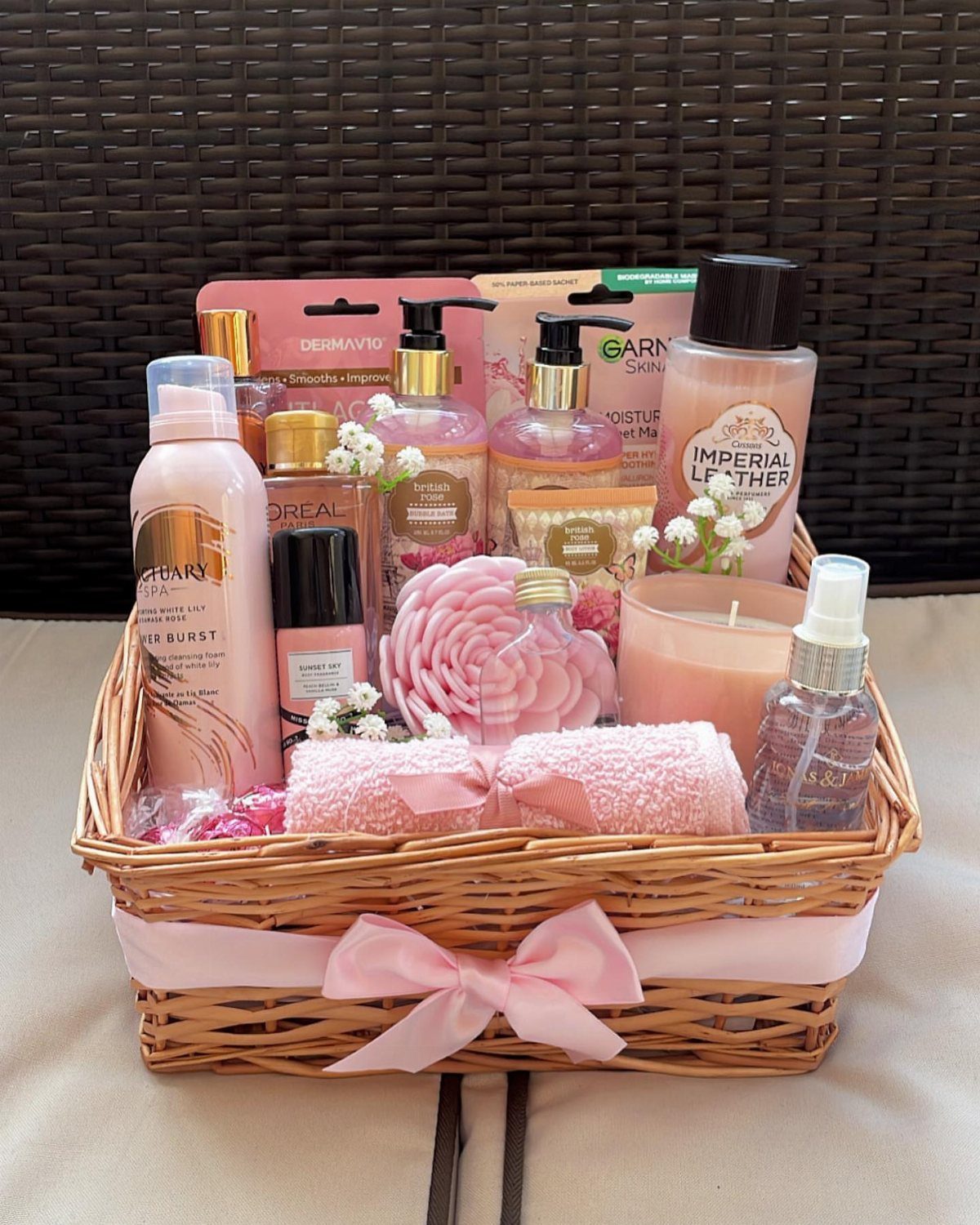 Wicker gift basket filled with pink skincare products, towels, and a scented candle.