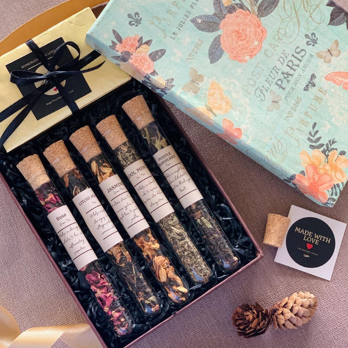 Assorted dried herbal tea blends in glass test tubes inside a gift box.