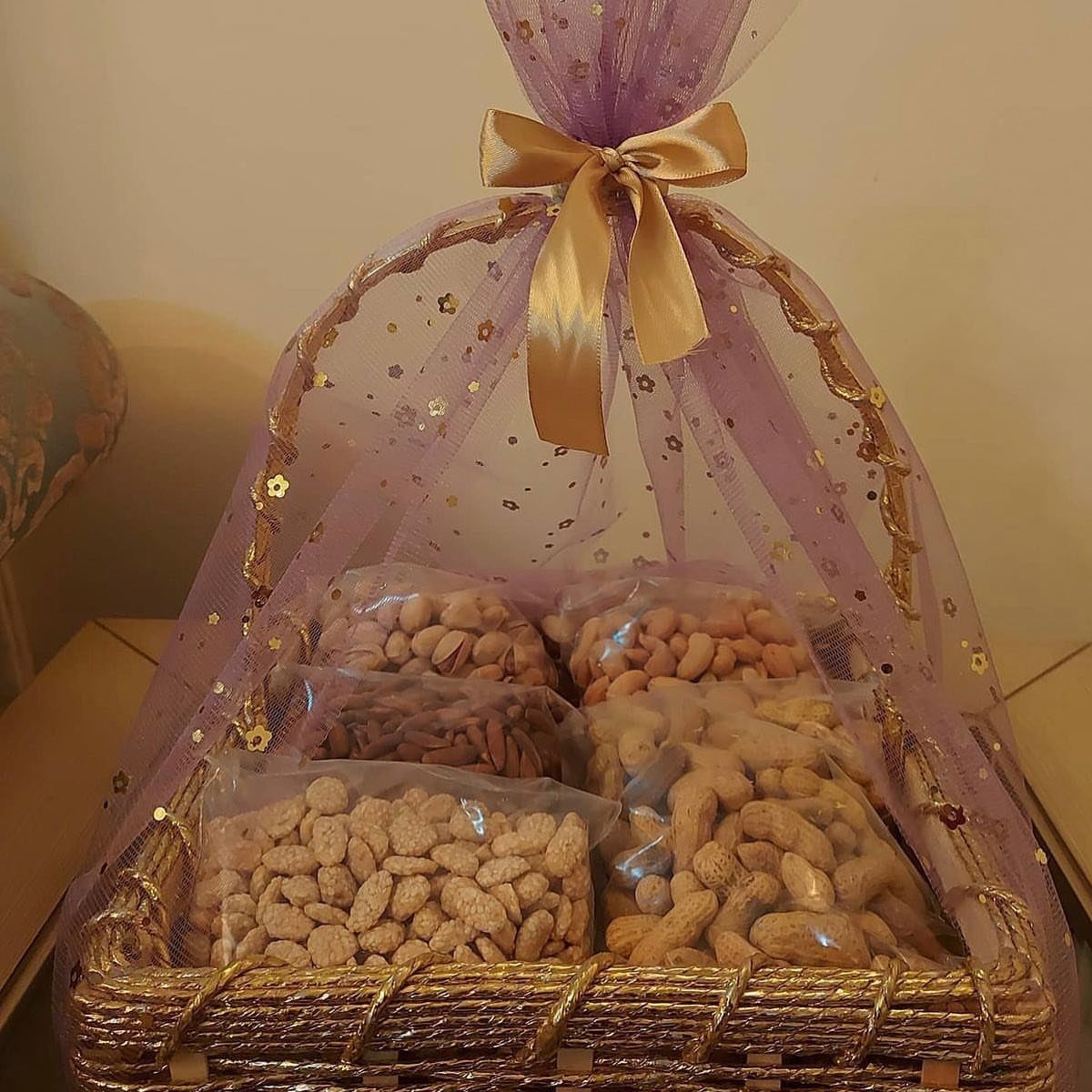 Wicker gift basket filled with bags of mixed nuts wrapped in purple tulle.