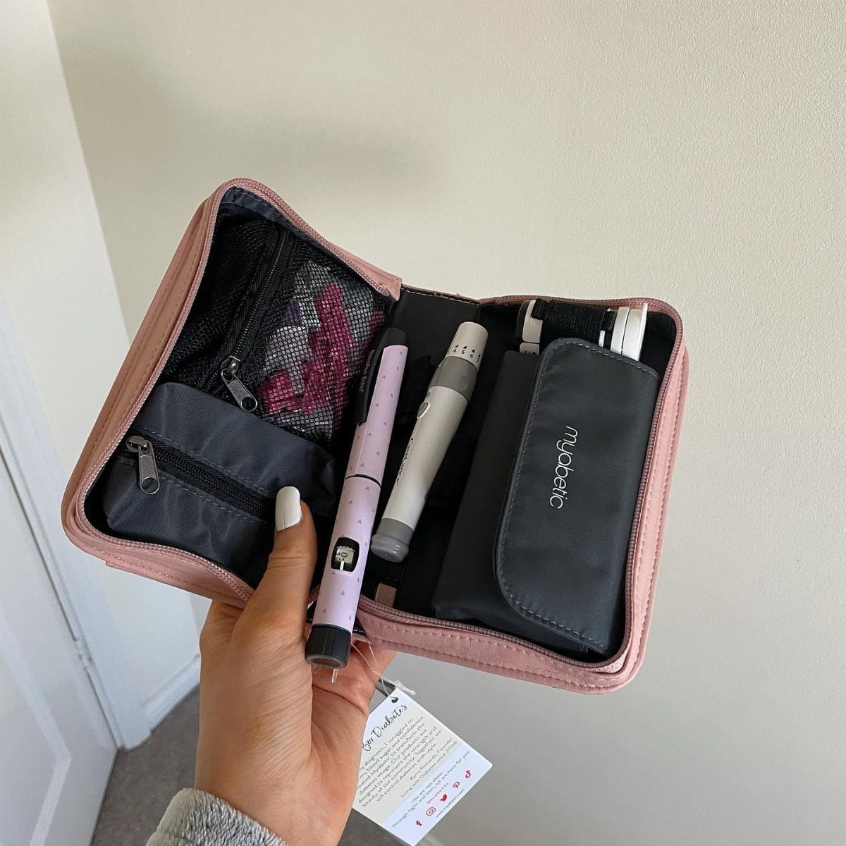 Pink portable diabetes supply case holding insulin pens and a glucose monitor.