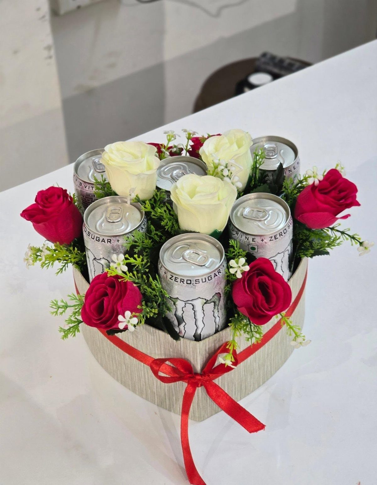 Zero sugar drink cans arranged with red and white roses in a gift box.