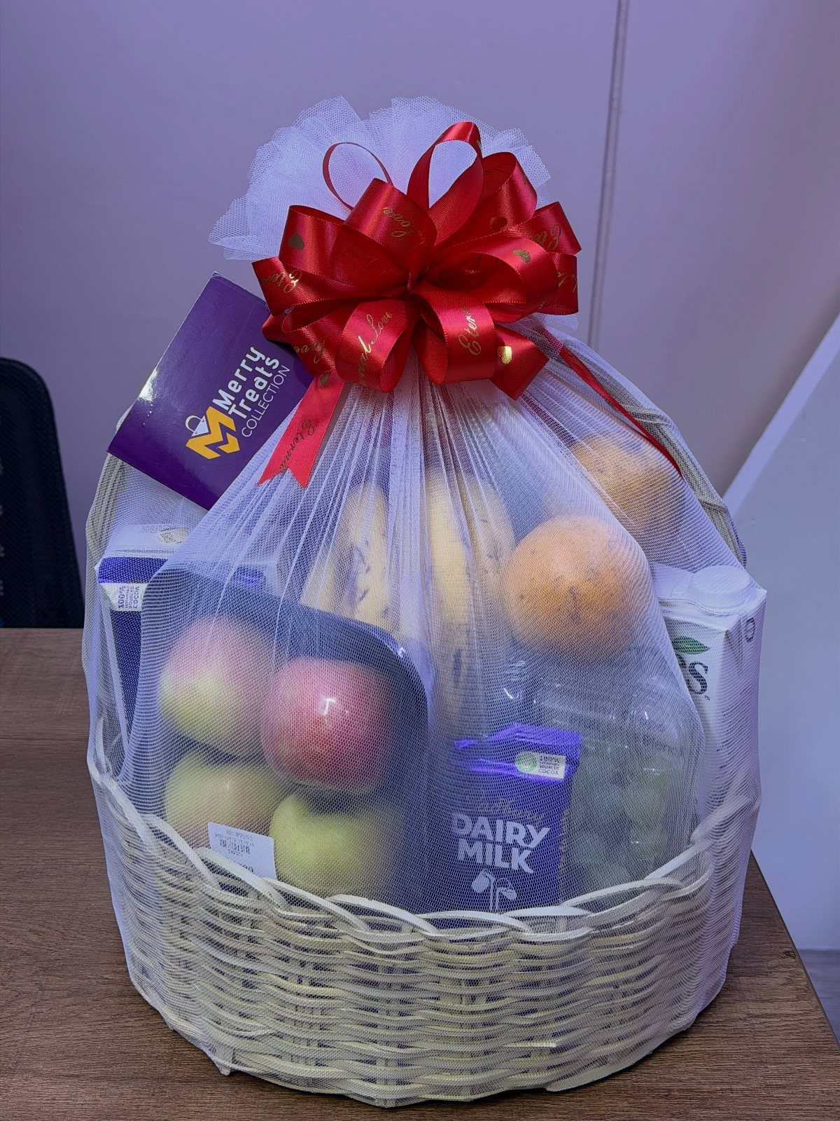 Gift Basket Ideas for Staff: 8 Picks From Wine to Coffee 3 Woven gift basket with fresh fruit and chocolate wrapped in white mesh netting.