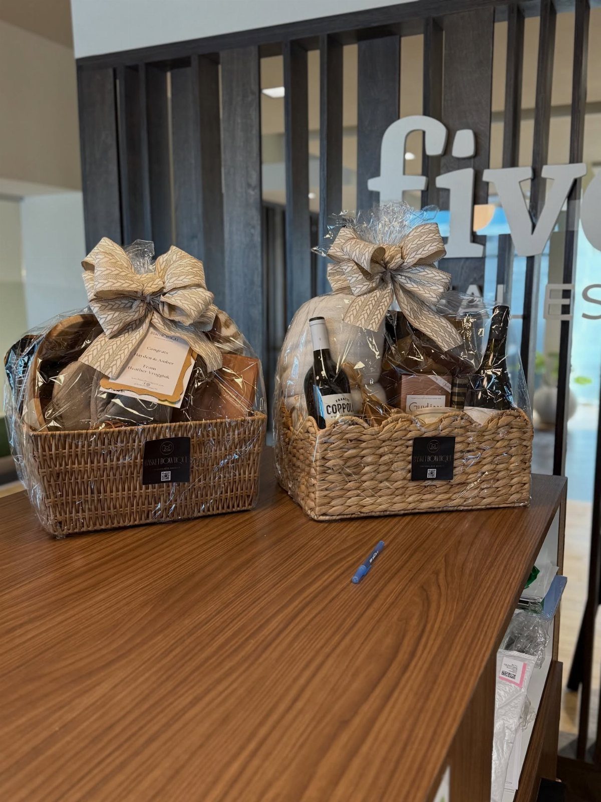 Gift Basket Ideas for Staff: 8 Picks From Wine to Coffee 4 Two cellophane-wrapped wicker gift baskets with burlap bows, one containing a wine bottle.