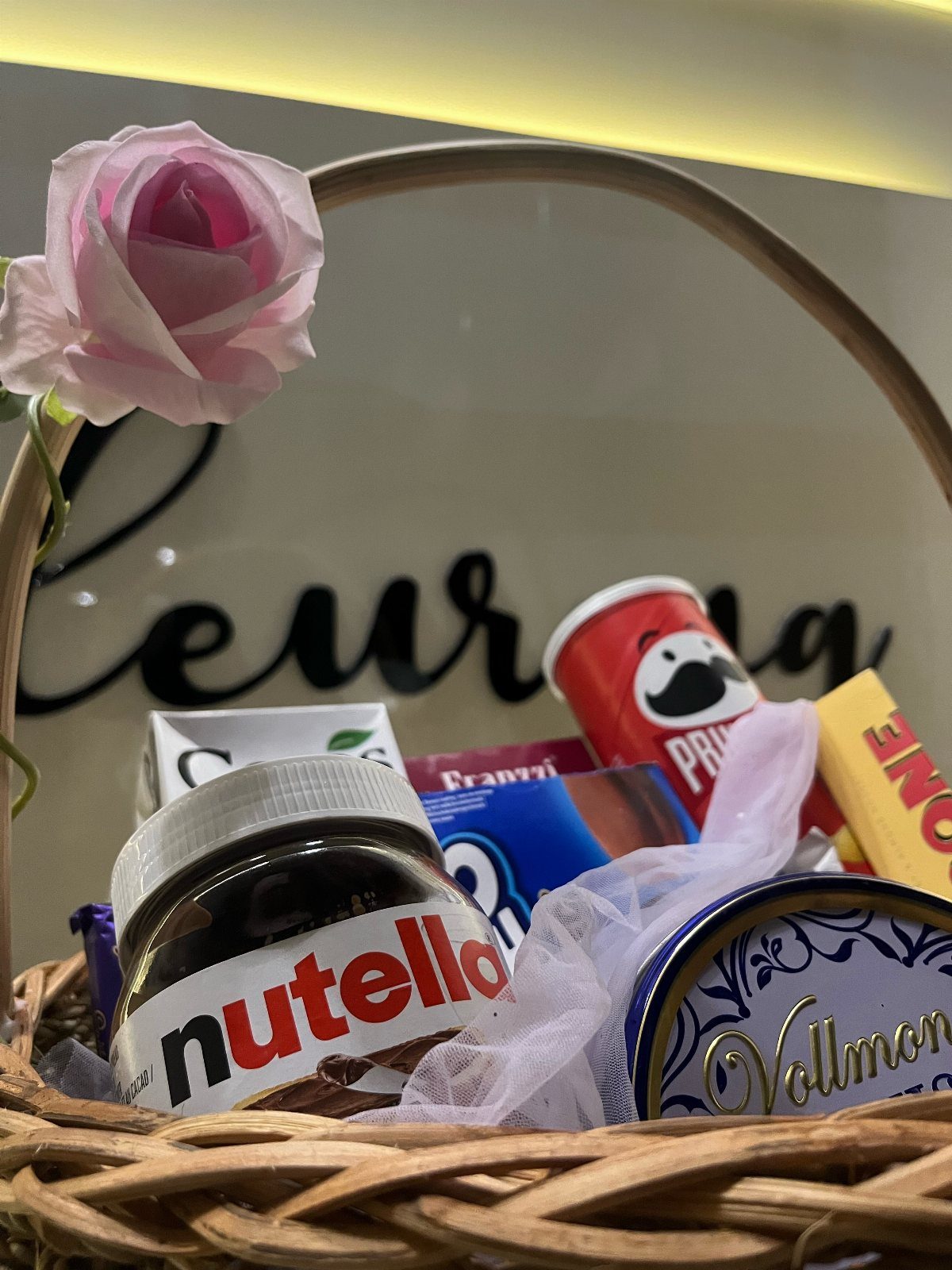 Wicker gift basket filled with Nutella, Pringles, and sweets with a pink rose.