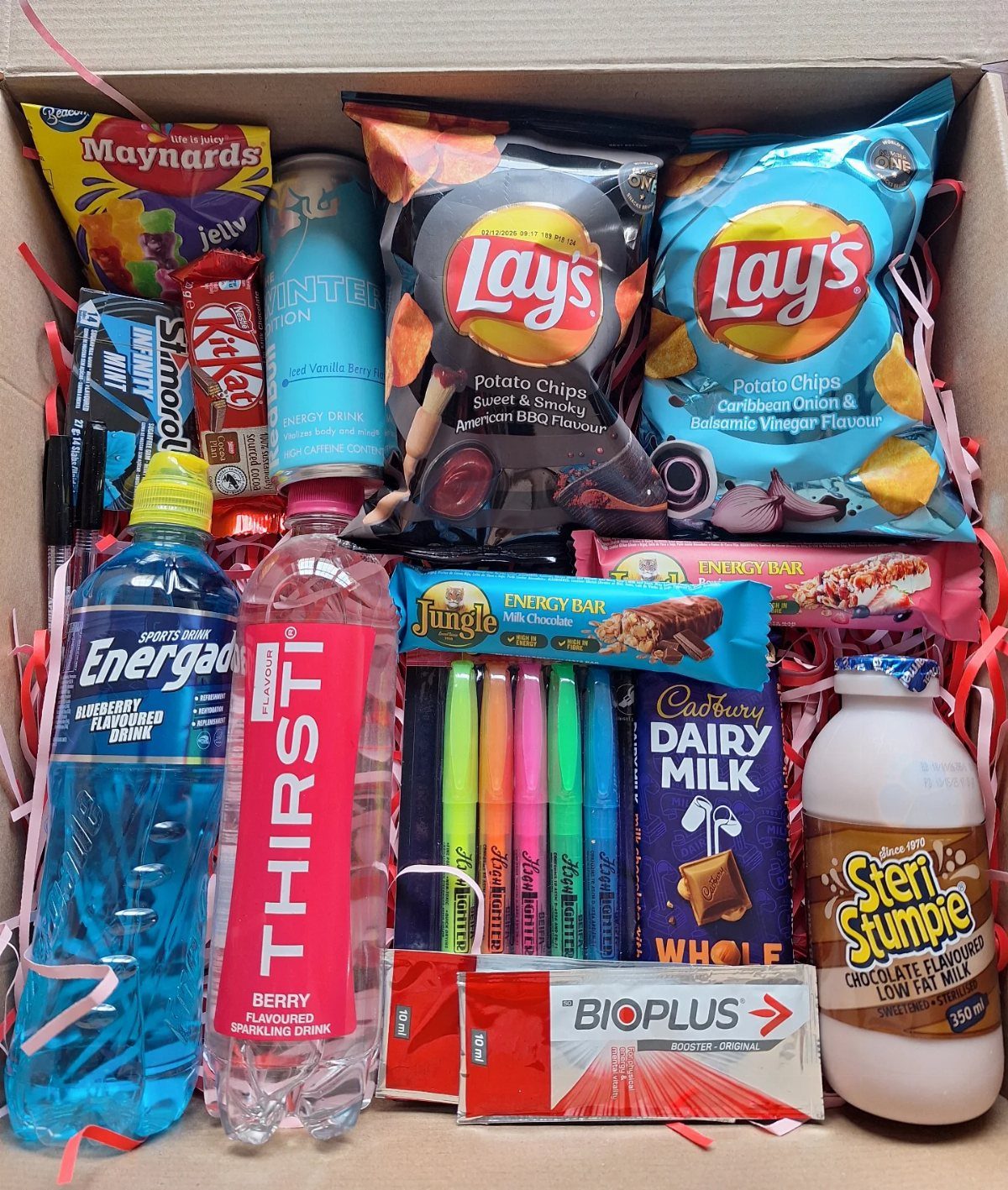 Gift basket in a cardboard box filled with snacks, drinks, and colorful markers.