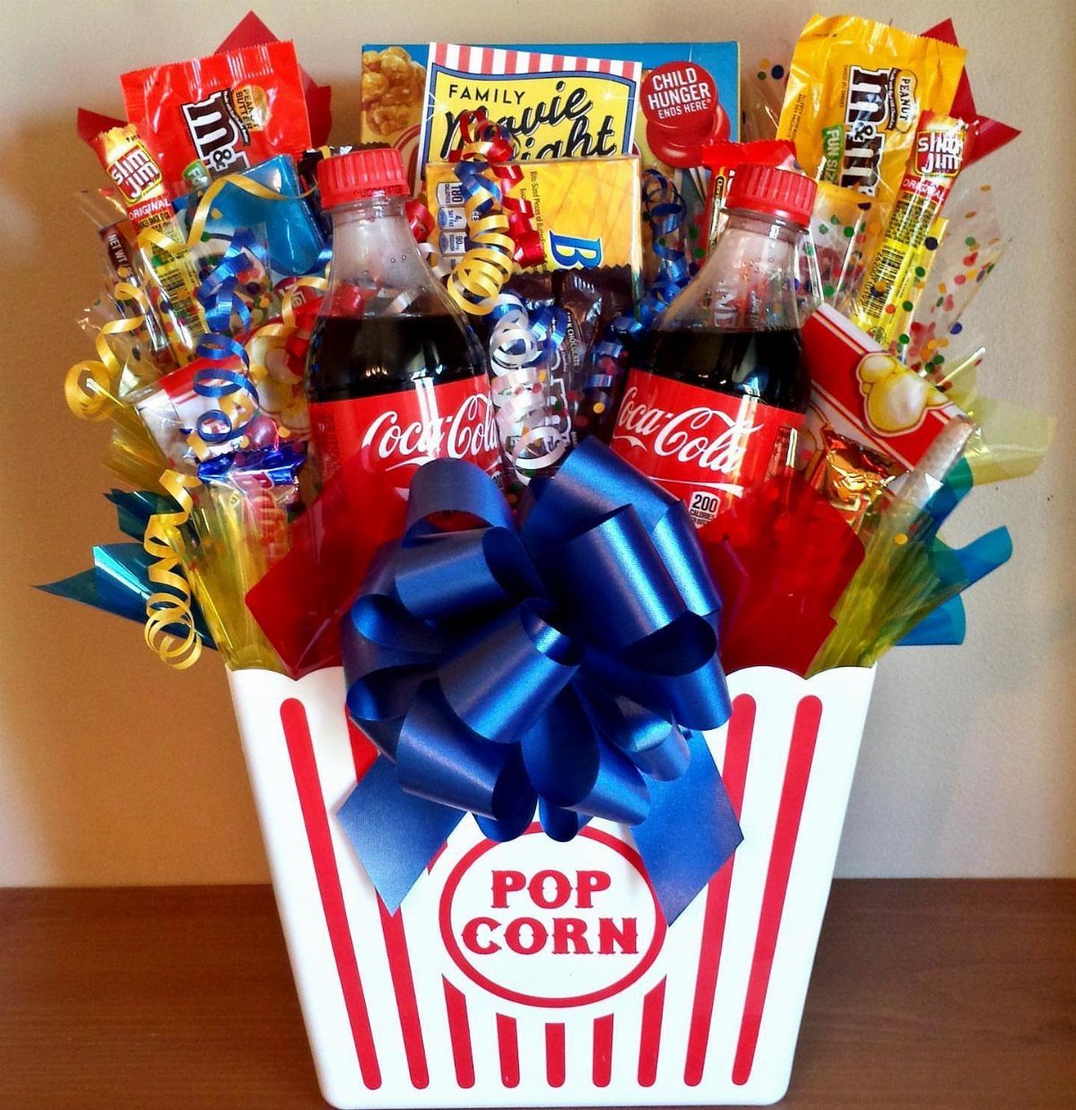 Popcorn bucket gift basket filled with soda, candies, and a large blue bow.