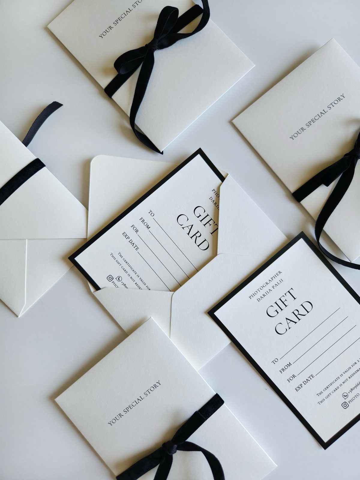 White gift cards and envelopes with black ribbons arranged on a white background.