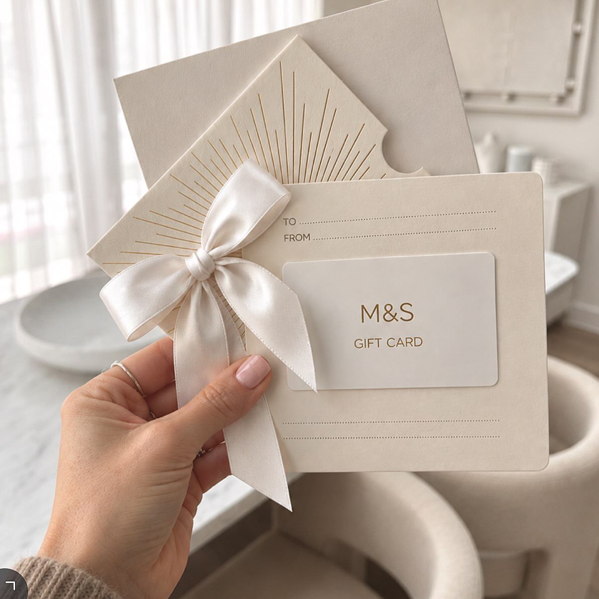 White greeting card with a white ribbon bow holding an M&S gift card.