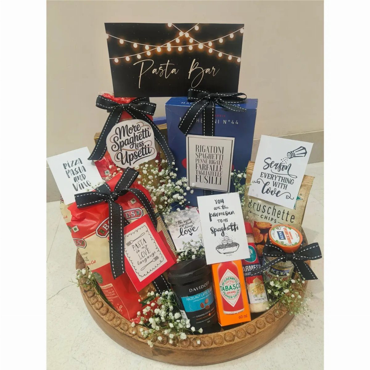 Gourmet pasta gift basket in a wooden bowl with condiments and decorative cards.