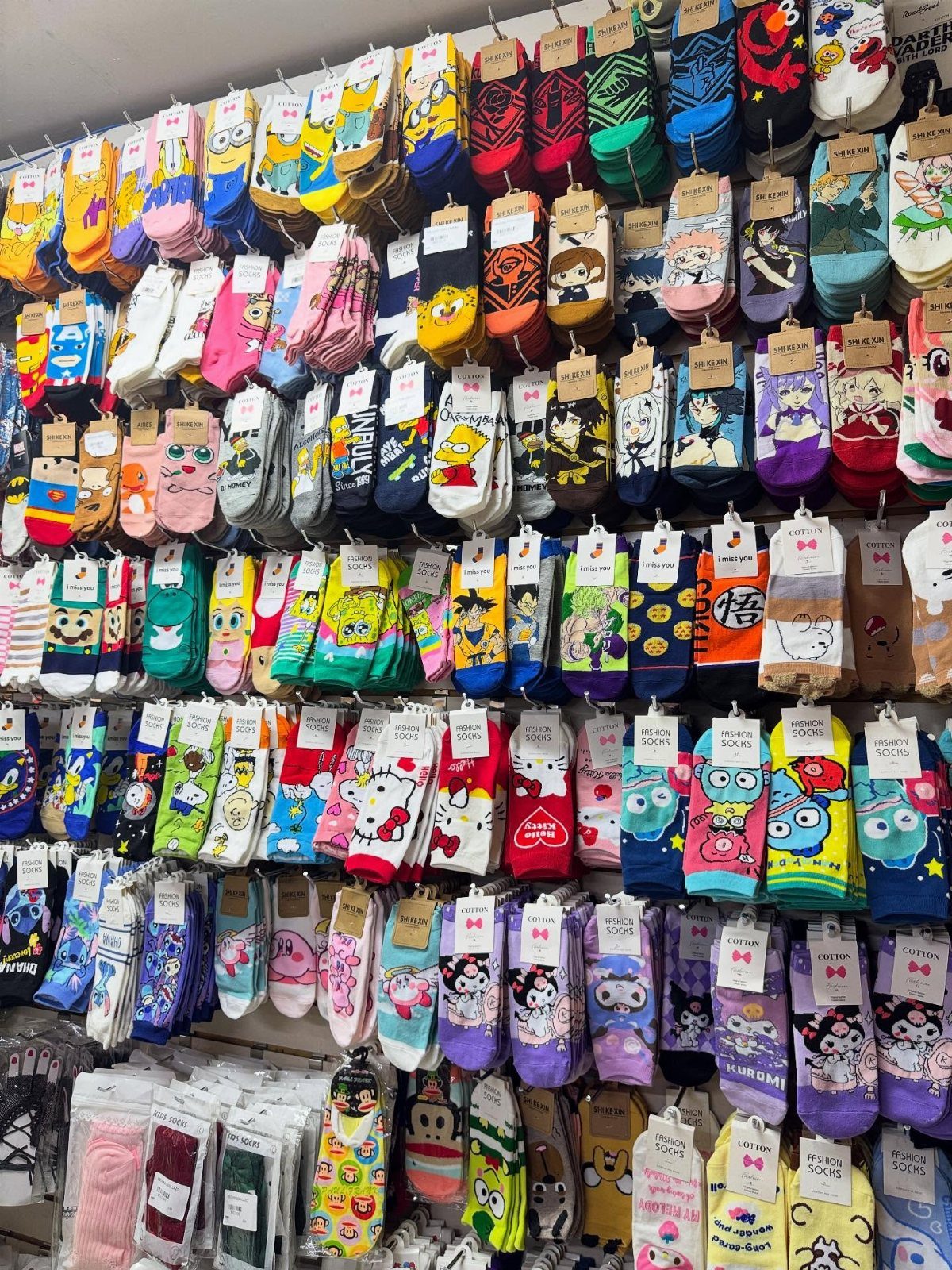 Colorful novelty socks with cartoon patterns hanging on a retail store display wall.