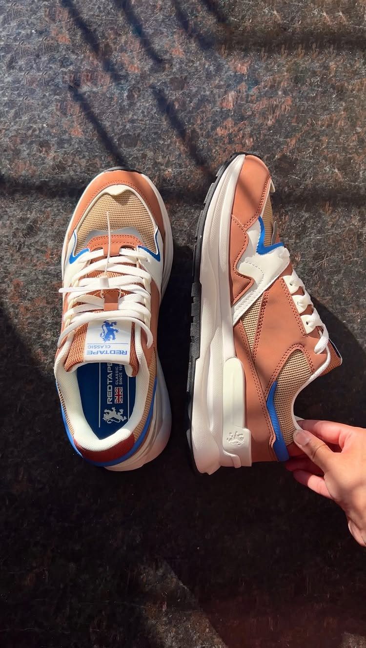 Brown and tan sneakers with blue accents on a dark stone surface.