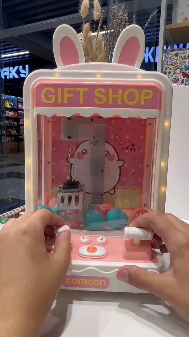 12 Gift Ideas for the Office Your Coworkers Will Use 7 Small pink toy claw machine with bunny ears being operated by two hands.