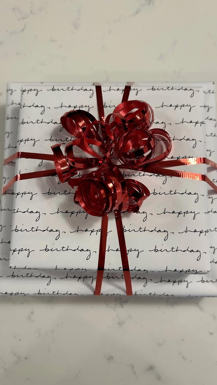 Gift wrapped in white birthday paper tied with a shiny red curly ribbon.