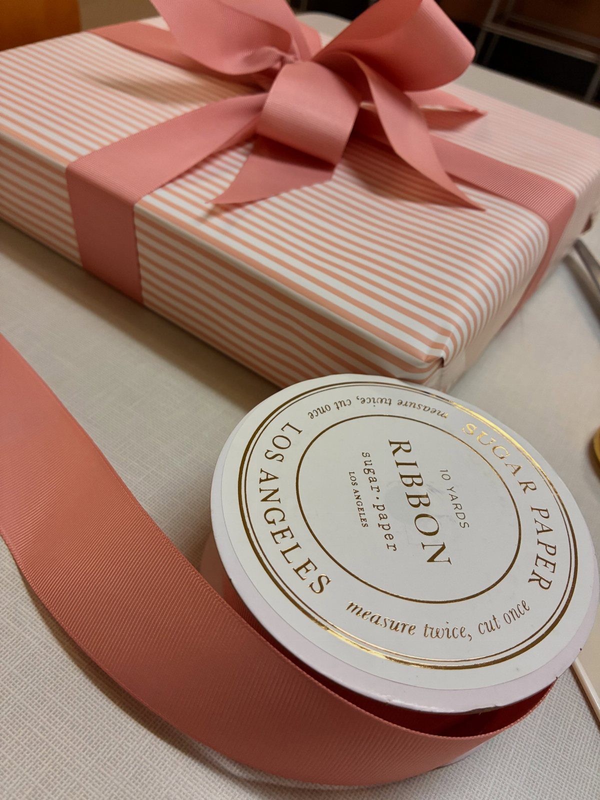 Pink striped gift box with a pink grosgrain ribbon bow and ribbon spool.