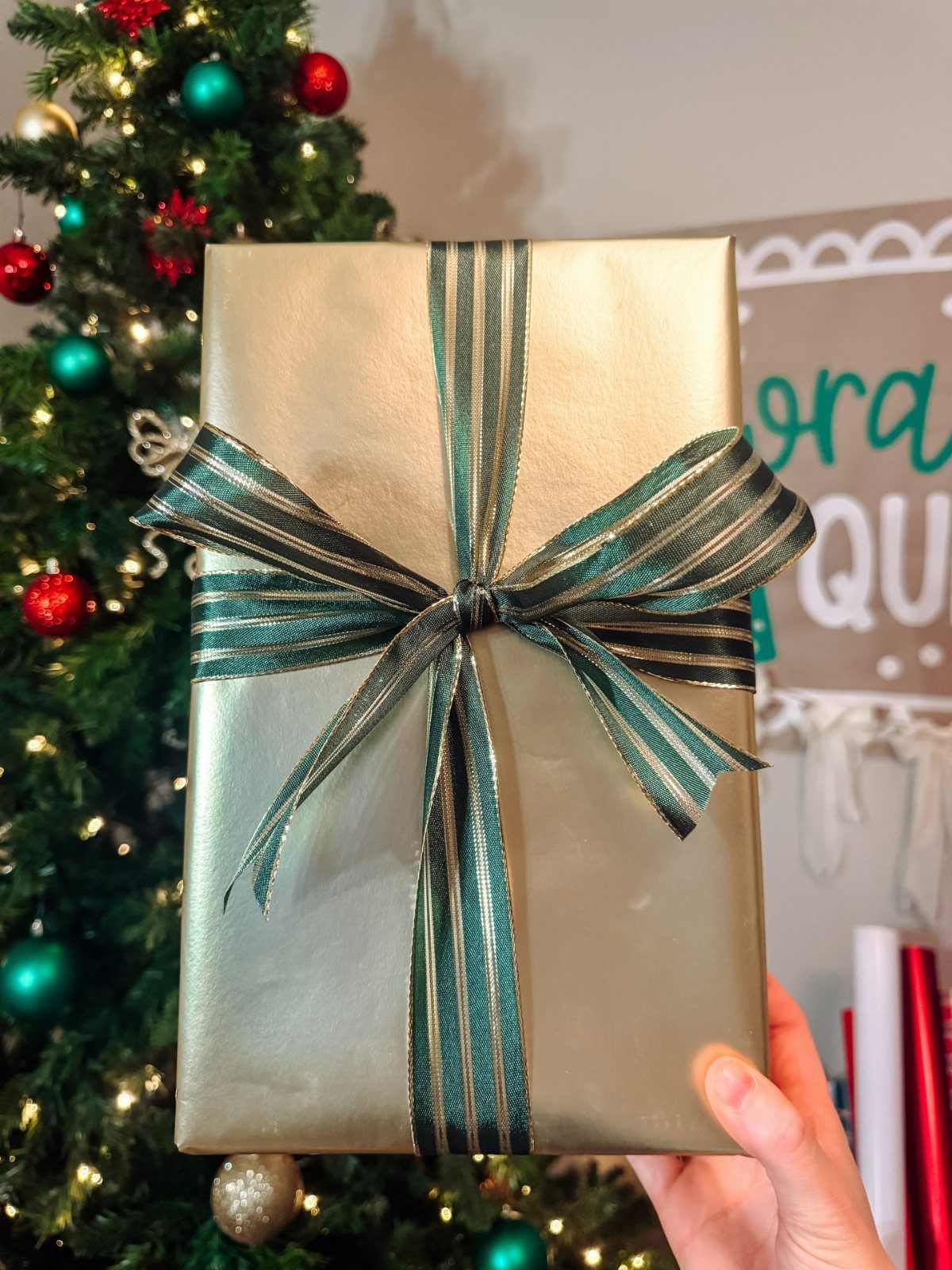 Gold wrapped gift box with a green and gold striped ribbon bow.