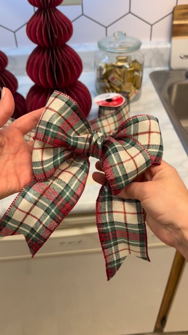 Plaid red and green fabric bow held by hands in a kitchen setting