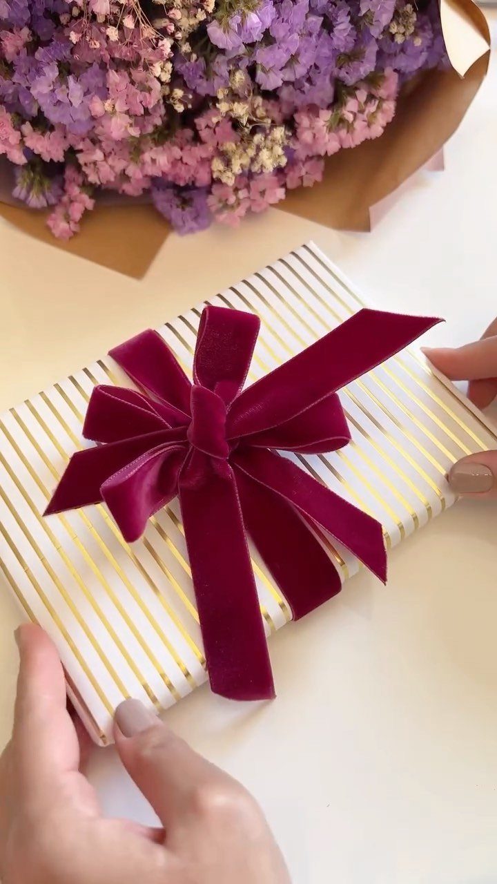 White and gold striped gift box tied with a burgundy velvet ribbon bow.