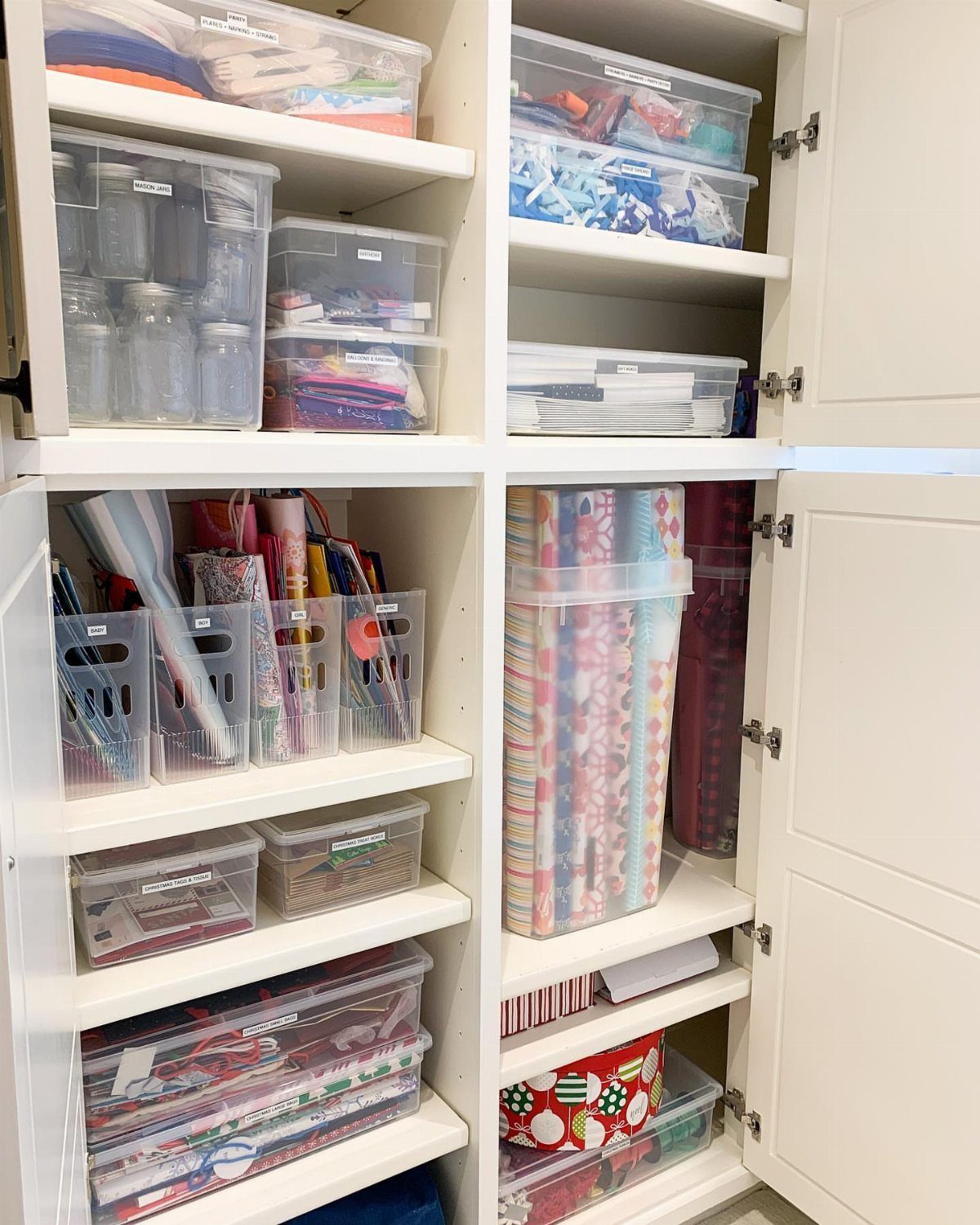 Organized white closet shelves with clear bins and colorful gift wrap rolls.