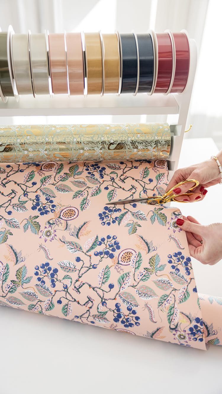 White storage rack with ribbons and wrapping paper being cut by gold scissors