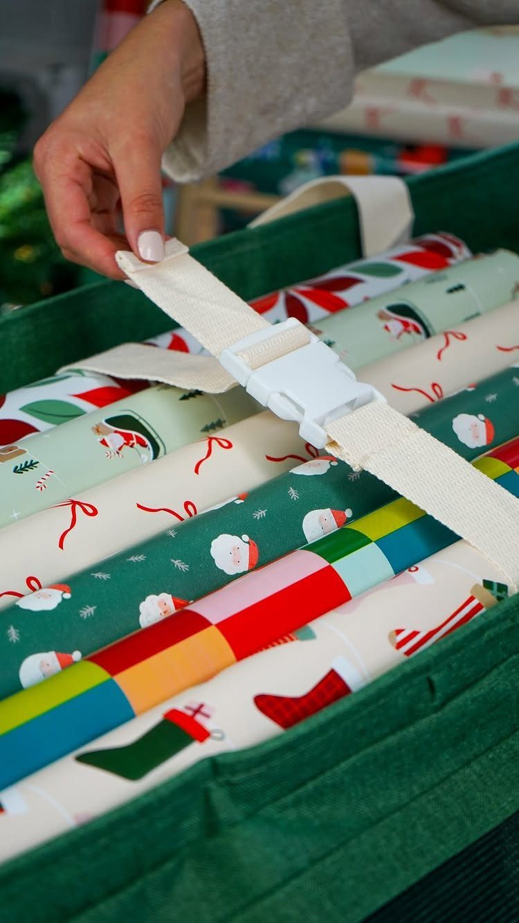 Green fabric storage bin filled with colorful Christmas wrapping paper rolls and white straps.