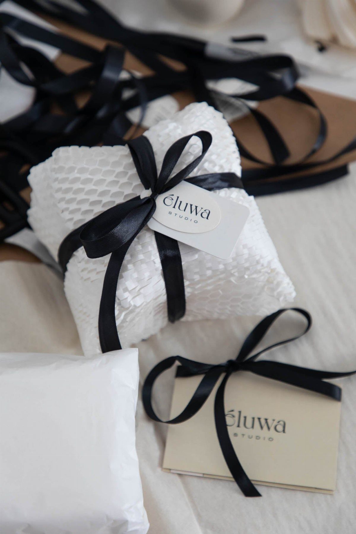 White textured gift box tied with a black satin ribbon and brand tag.