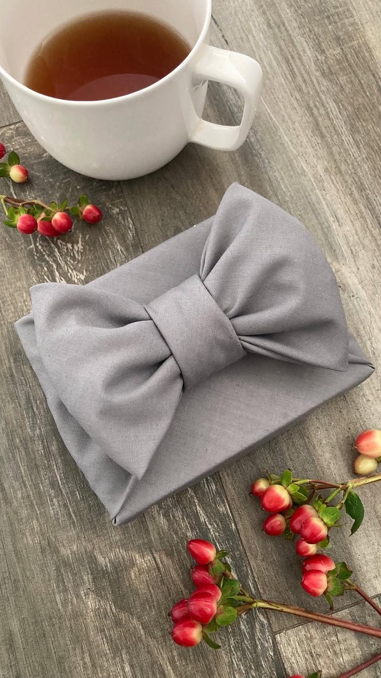 Grey fabric wrapped gift with a bow next to tea and red berries