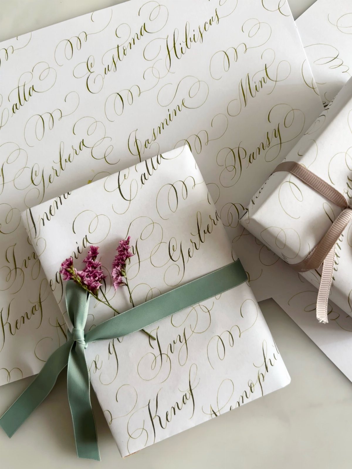 Gifts wrapped in white paper with gold calligraphy and a sage green ribbon.