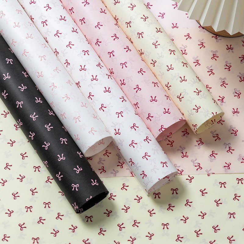 Rolls of wrapping paper in various colors with a red bow pattern.