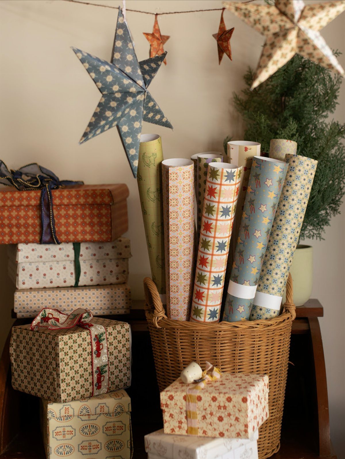 Wicker basket filled with patterned wrapping paper rolls and wrapped gift boxes.