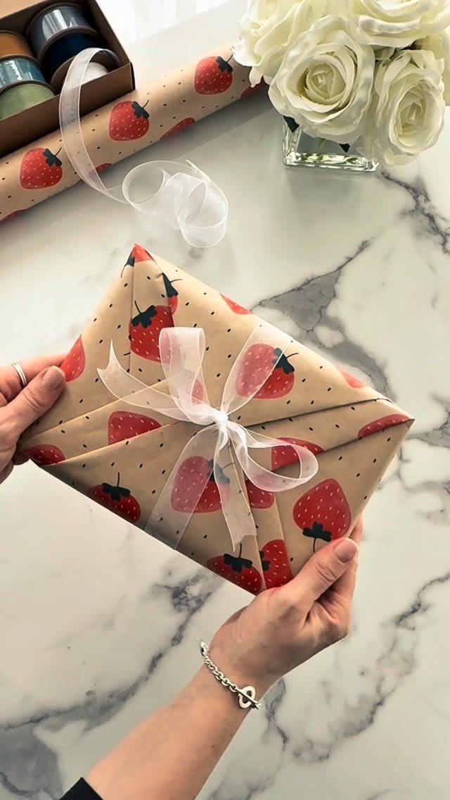 Wrapped gift with strawberry pattern paper and white ribbon held by two hands