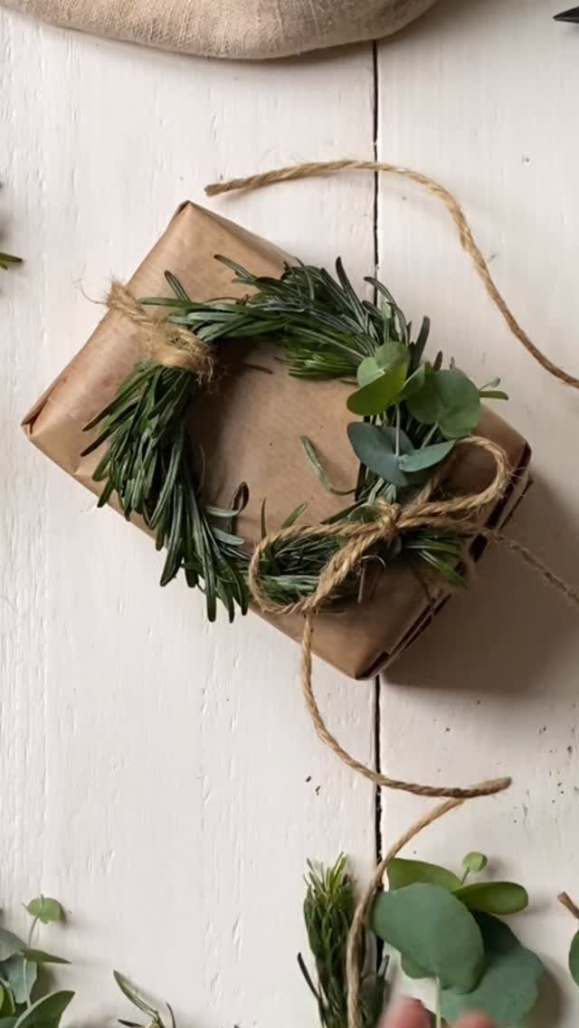 Brown paper wrapped gift topped with a small green rosemary and eucalyptus wreath.