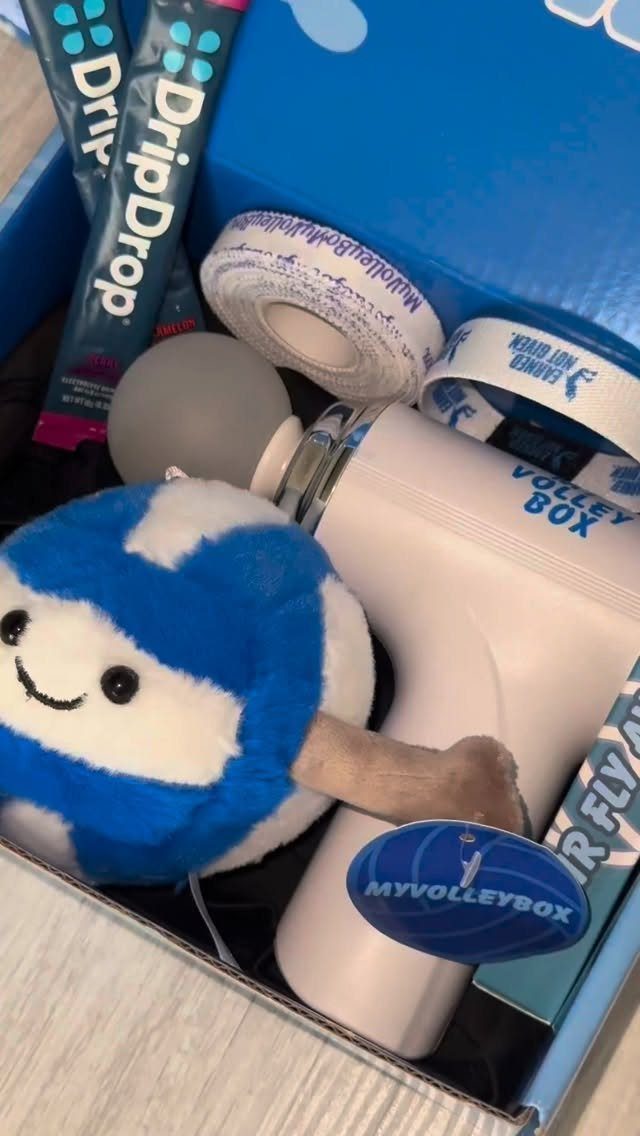 Blue gift box containing a massage gun, plush volleyball, and hydration packets.
