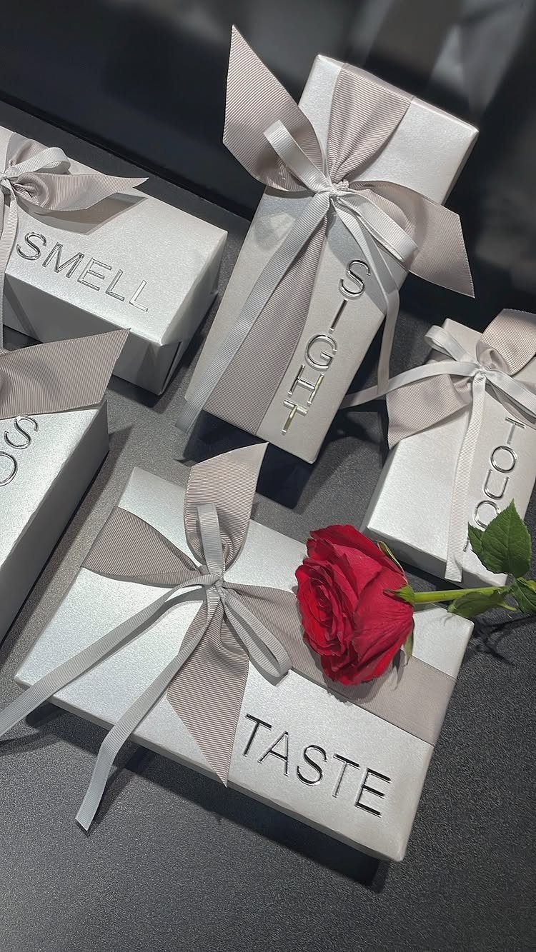 White gift boxes labeled with the five senses, accompanied by a red rose.
