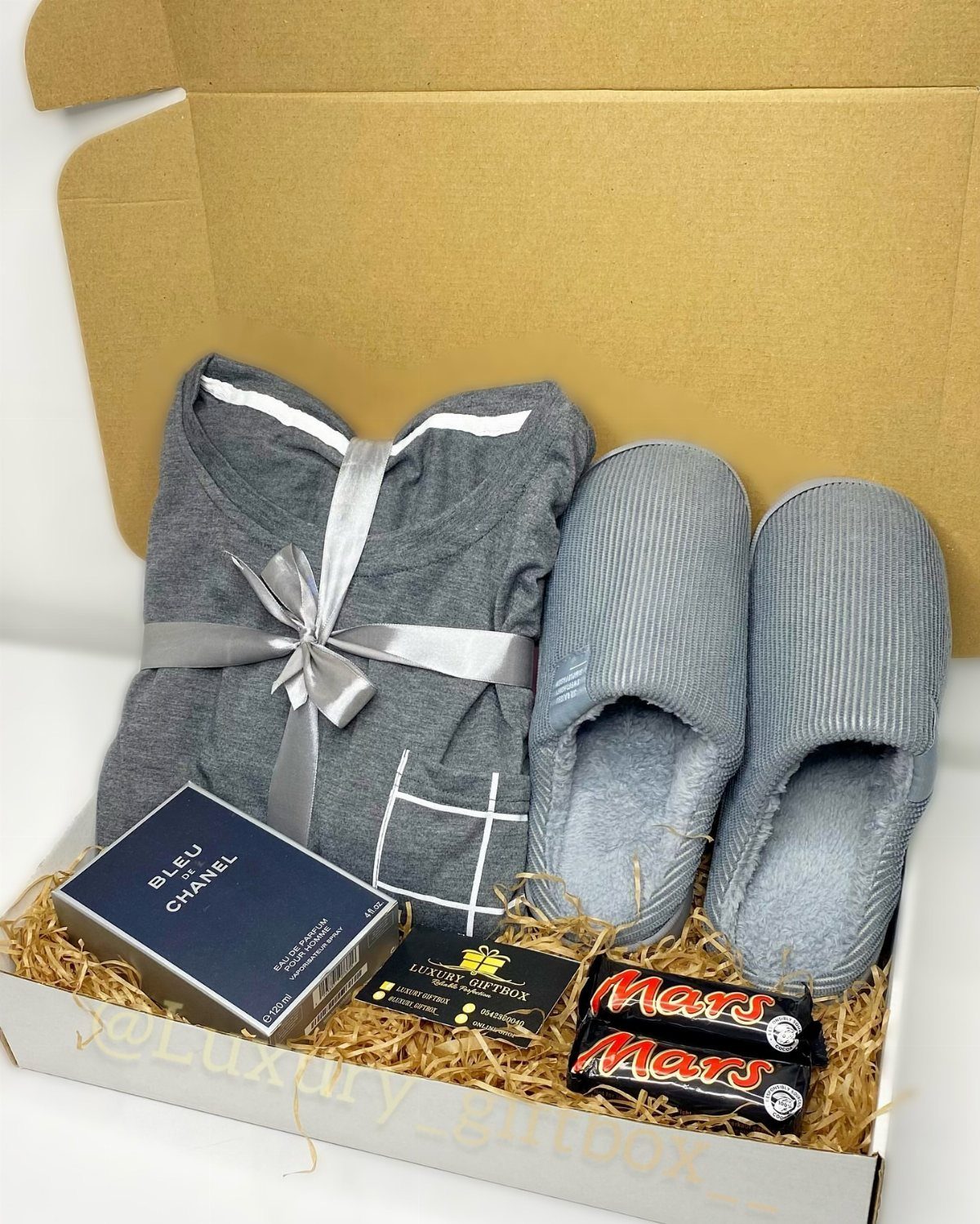 Gift box with grey loungewear, slippers, Chanel cologne, and Mars chocolate bars.