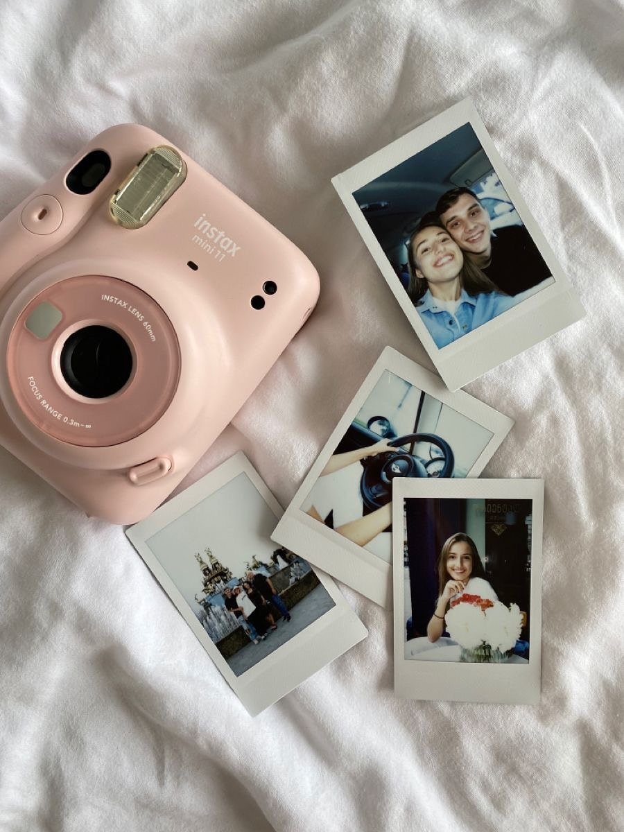Pink instant camera and polaroid photos on a white fabric background