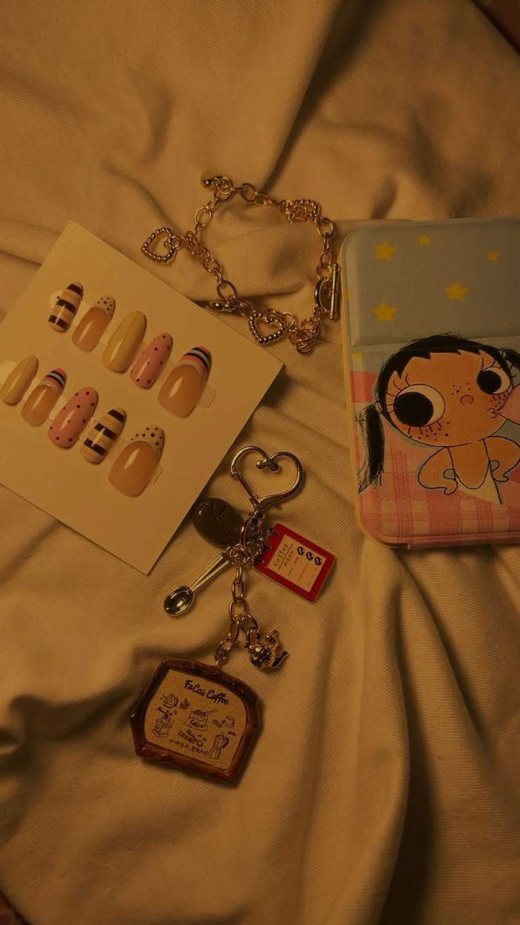 Press-on nails, gold bracelet, and cartoon phone case on white fabric.