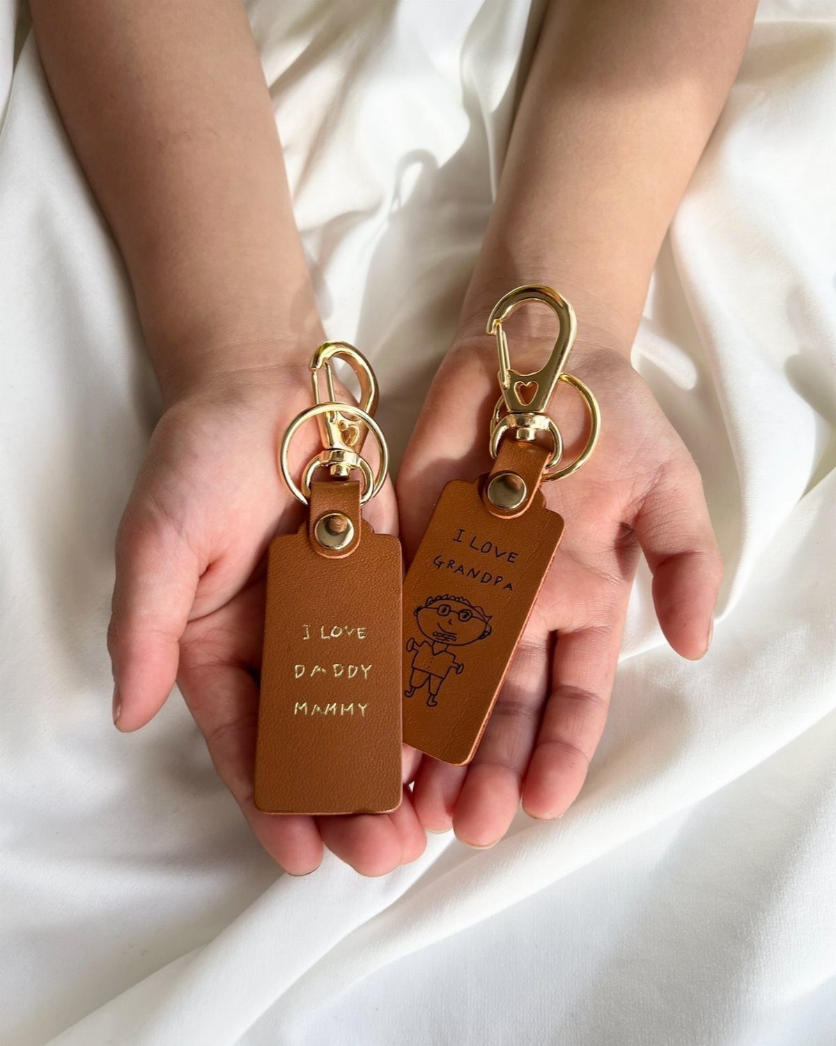 6 Gifts for Grandpa Who Has Everything: Personal Picks 3 Two brown leather personalized keychains held in a child's open palms.