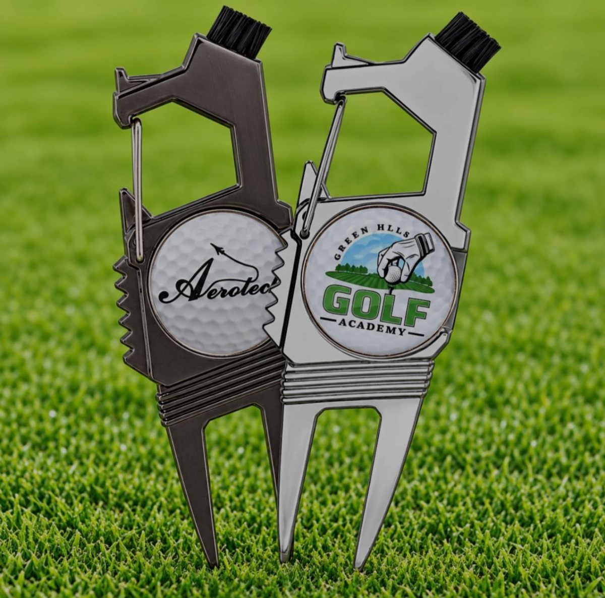 Two metal golf divot tools with custom logos standing in green grass.