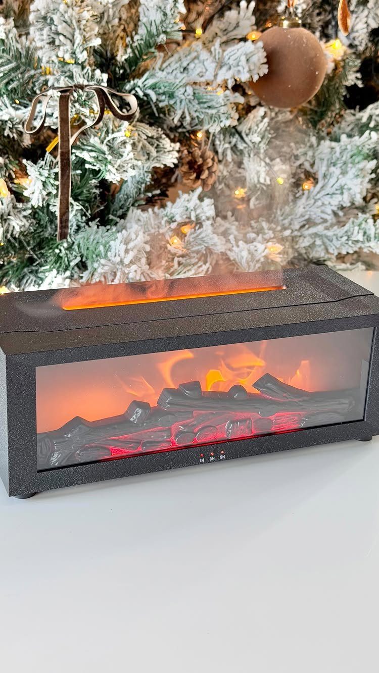 Mini electric fireplace with glowing logs and steam in front of a Christmas tree