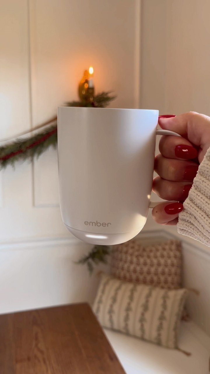 White Ember smart mug held by a hand with red nail polish indoors.